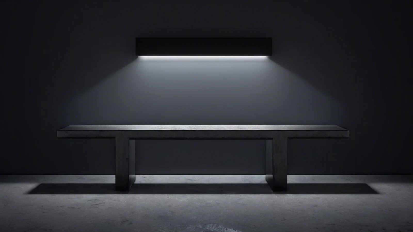 A single cold lamp mounted high on a dark wall, its light falling across the middle of a long bare concrete bench while both ends of the bench recede into grey shadow.